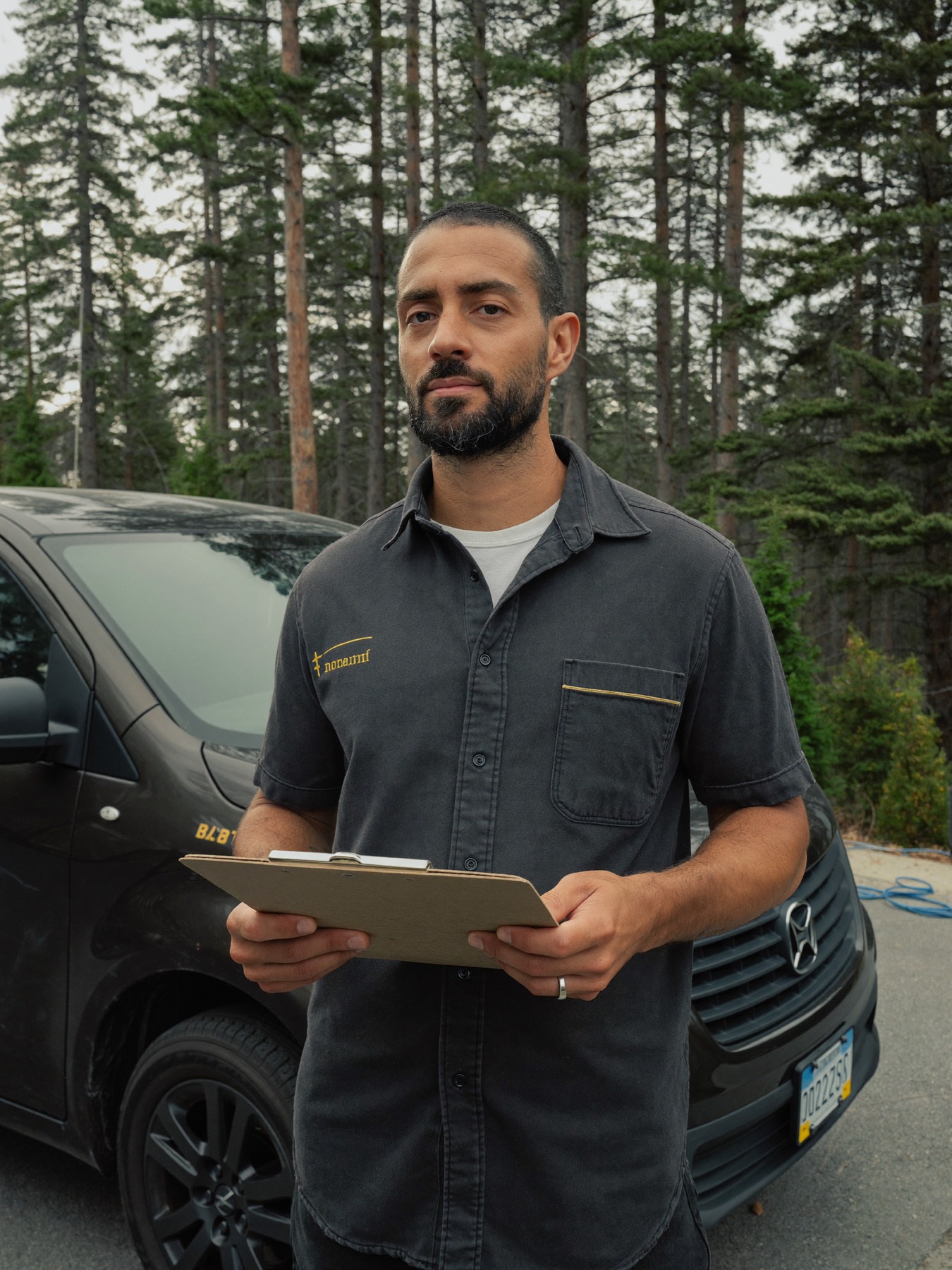 Ray Alder, the fictional owner and master electrician, standing by his van under ponderosa pines